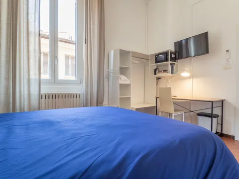 Schlafzimmer mit blauer Tagesdecke und Schreibtischbereich